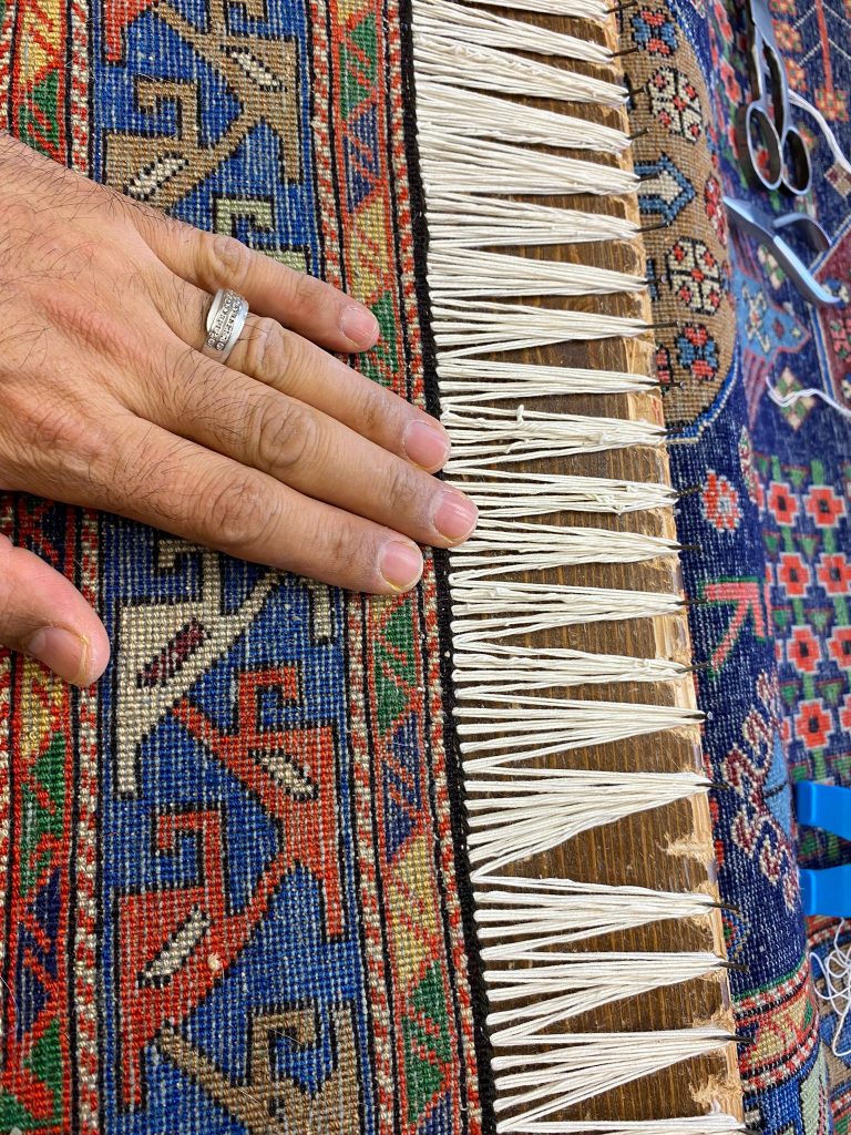 Nuove frange annodate a mano su un tappeto persiano nel laboratorio Art Tappeti di Milano