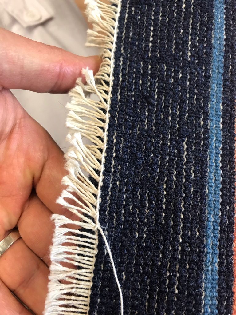 Frange sfilacciate di un tappeto blu riparate a mano a Milano