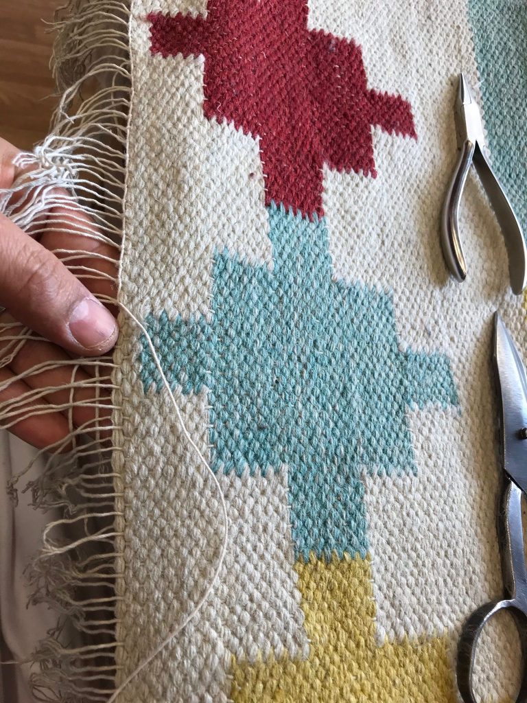 Rifacimento delle frange di un kilim a motivi geometrici con le pinze da restauratore a Milano